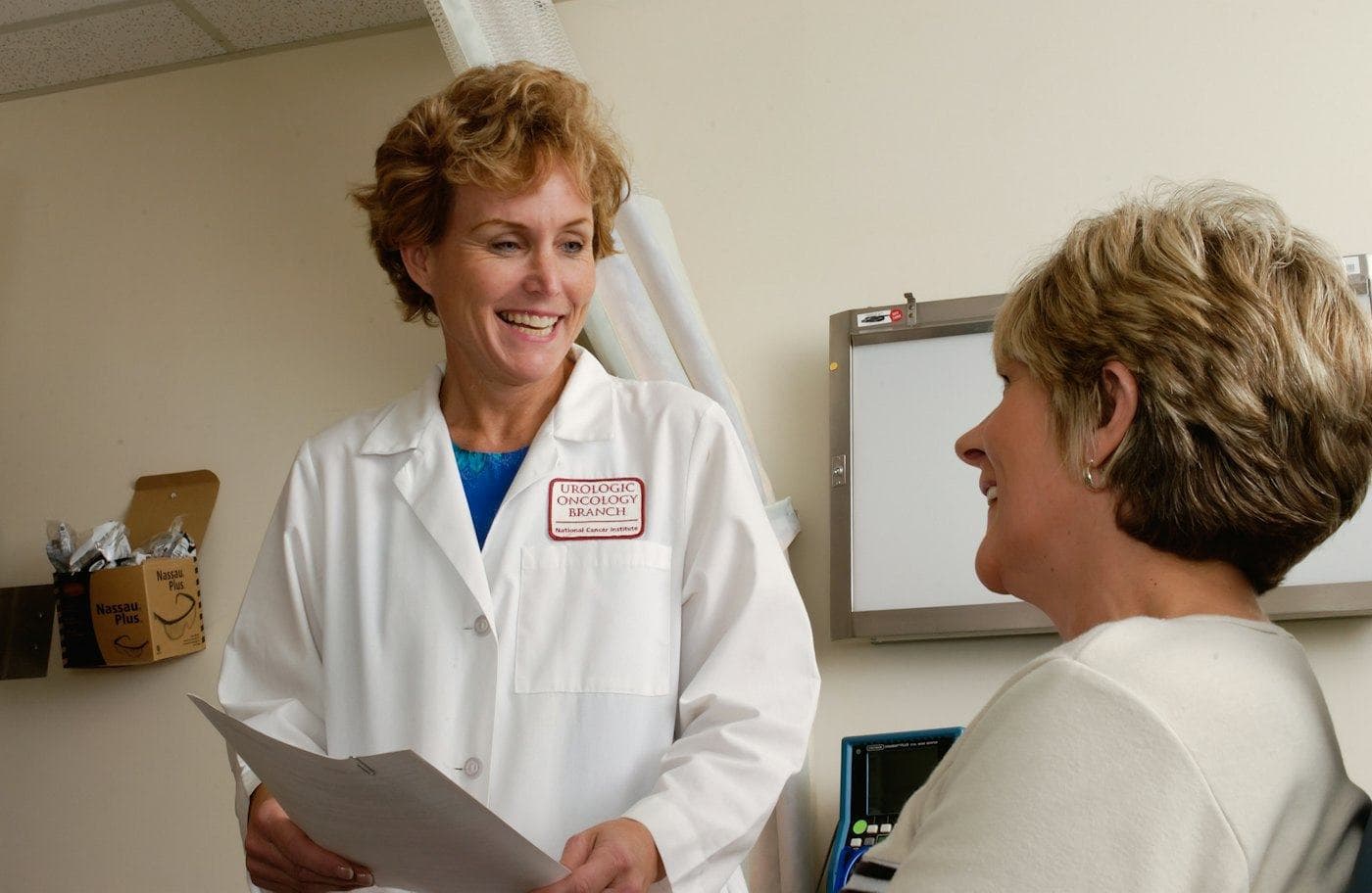 A smiling doctor in a white coat holding notes while talking with a patient
